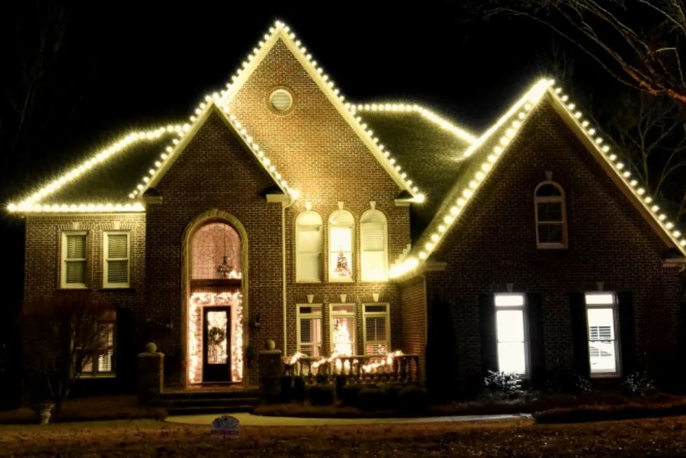 Dark brick house with steep gables outlined in light above an arched front entry.