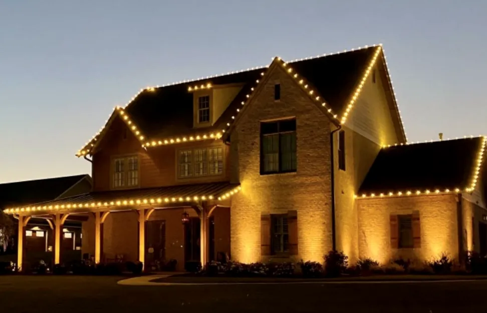 Brick house with a covered porch lit in warm white lights at dusk.