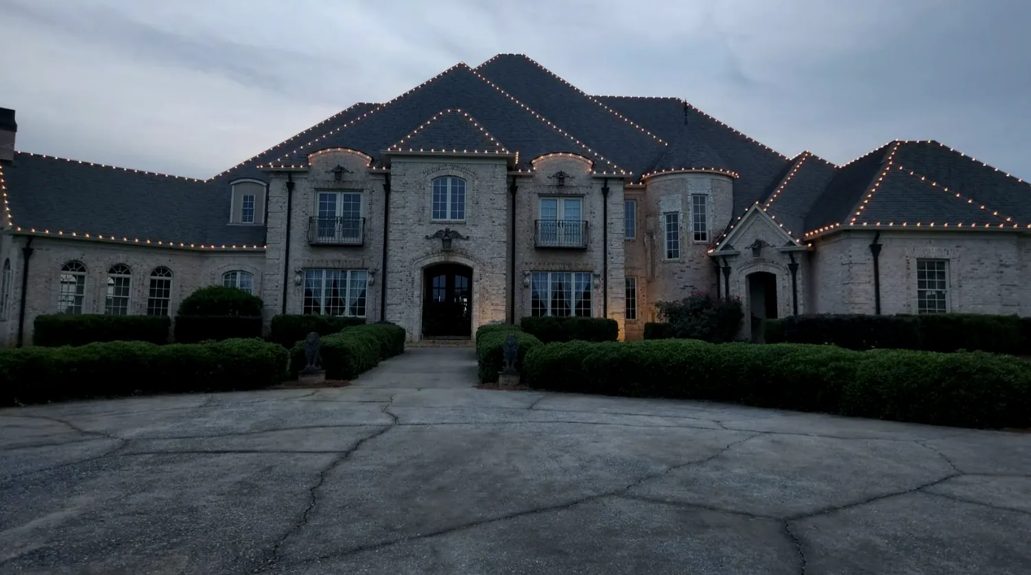 Large stone house with many roof peaks and a wide circular drive at dusk.