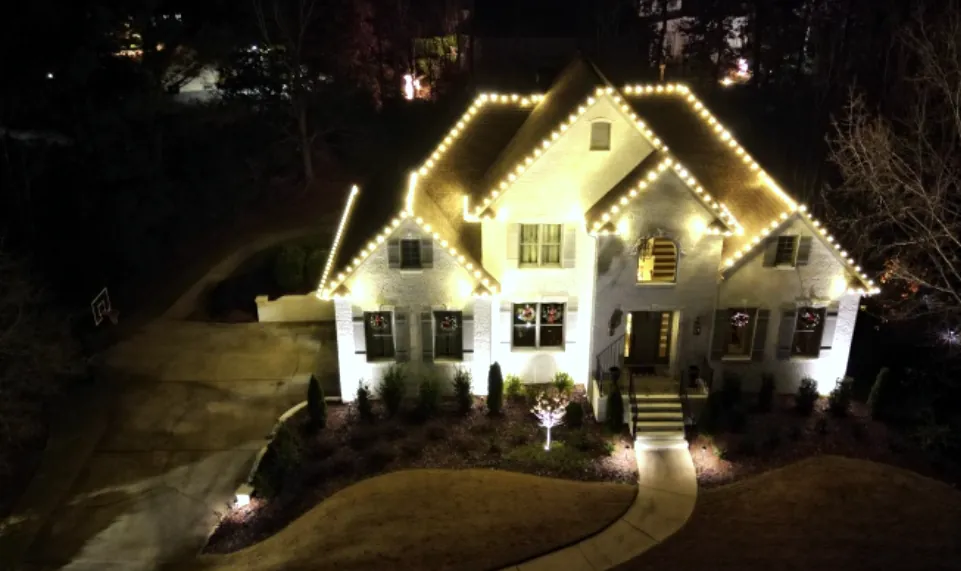 White house photographed from above with a lit roofline and a curved driveway below.